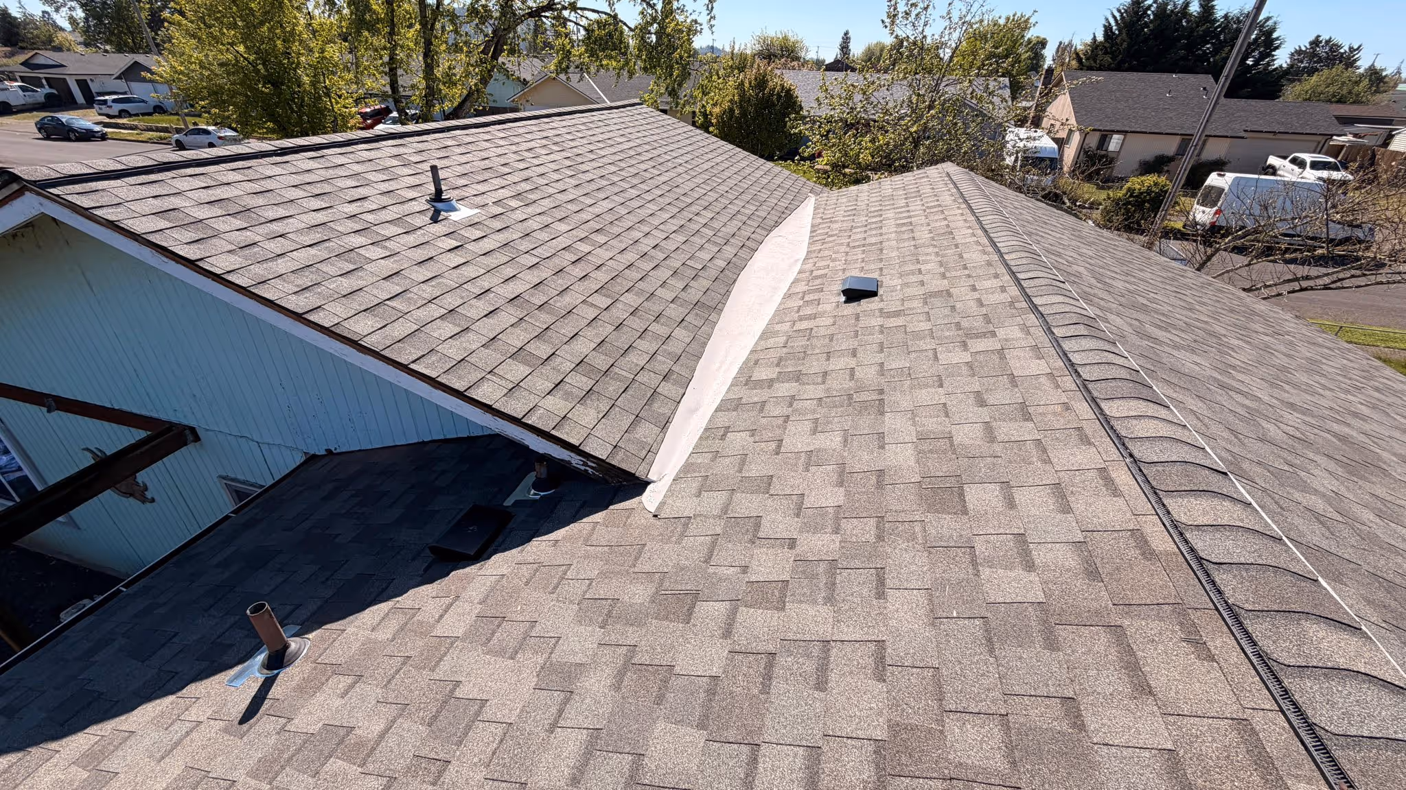 Shingled rooftops of residential houses with vents and a clear sky in the background.
