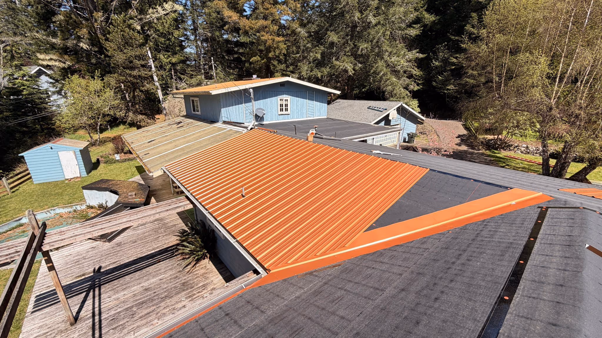 A house roof under construction with new corrugated metal panels partially installed and black roofing felt visible.