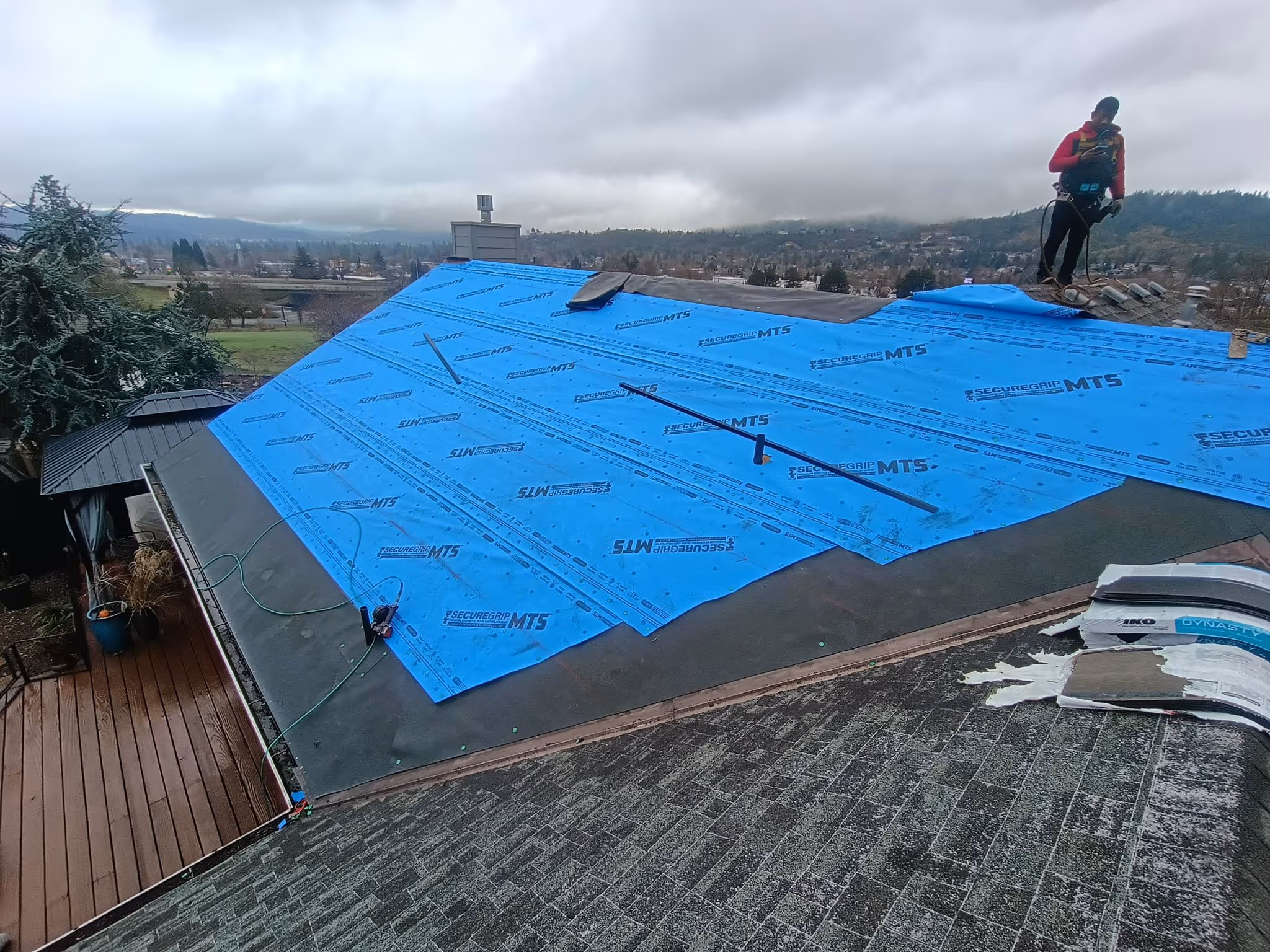 Construction worker standing on a roof covered with blue underlayment sheets during roofing replacement on a cloudy day.