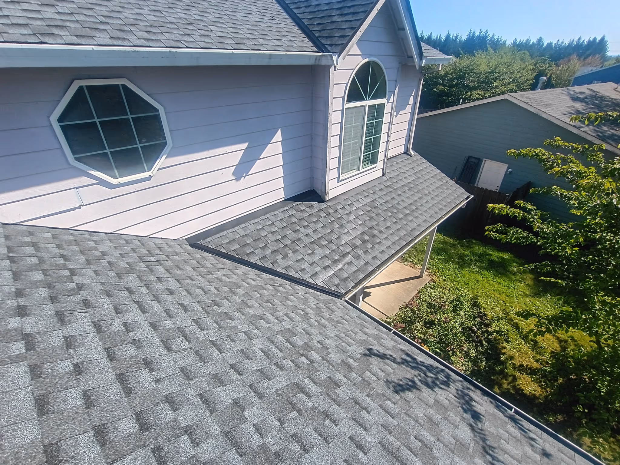 View of a house roof with gray asphalt shingles, featuring an octagonal window and an arched window.