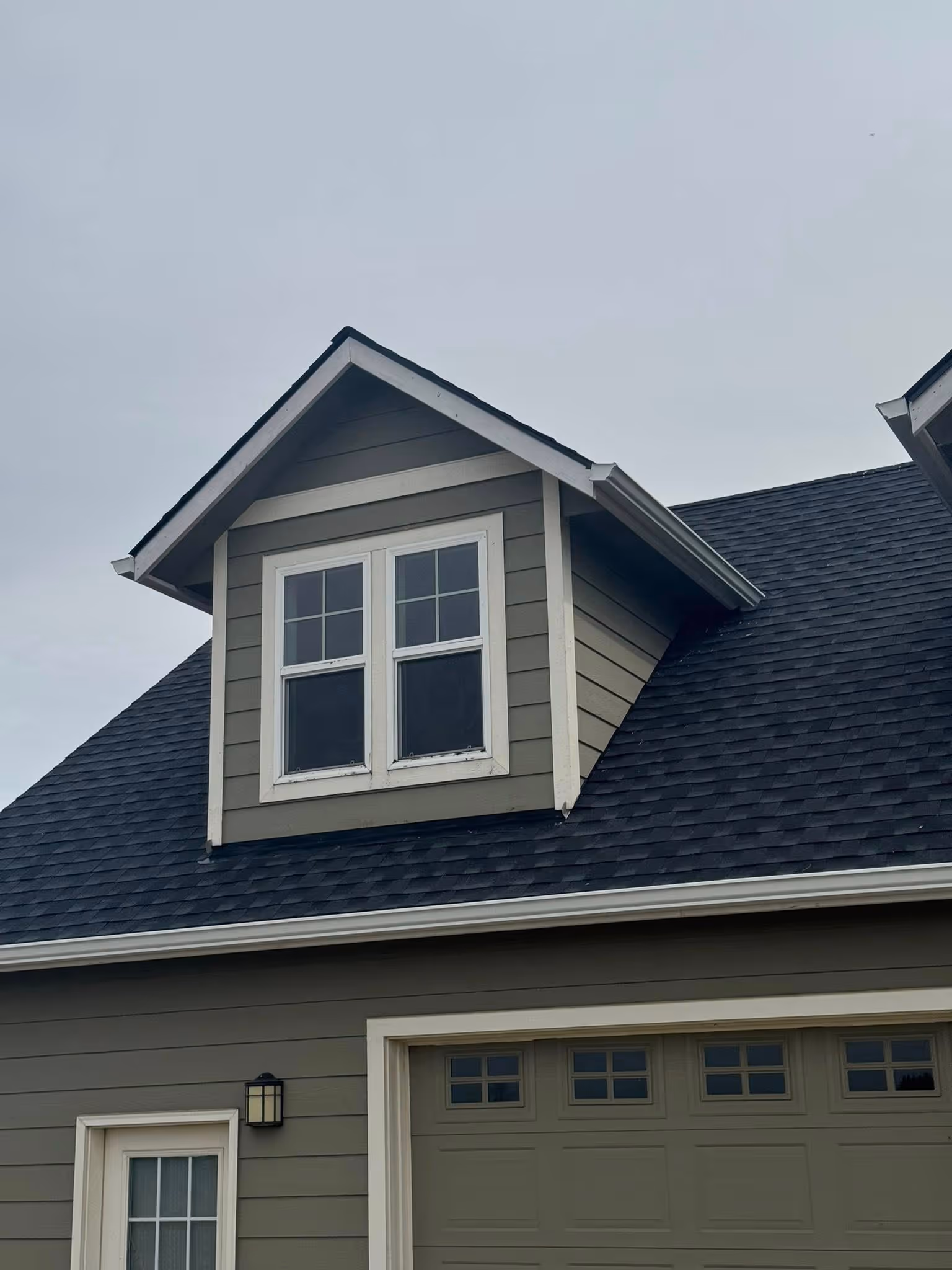 Grey house exterior showing a gable window above a garage door with small windows, under an overcast sky.
