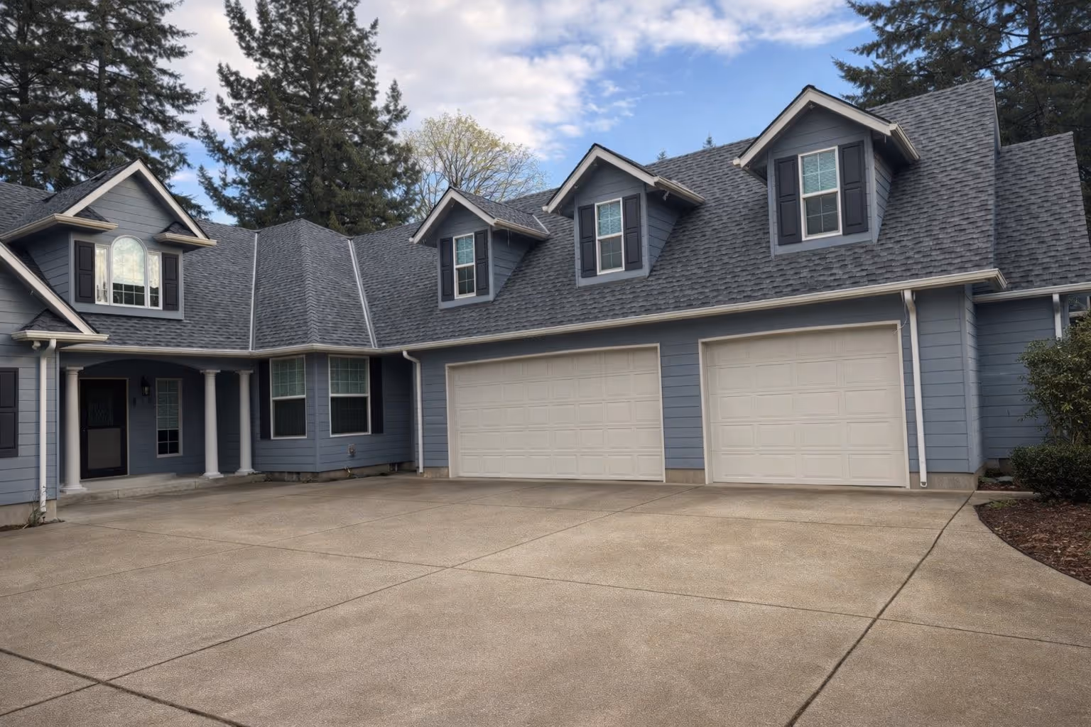 Blue two-story house with three dormer windows, white columns at entrance, and double garage doors.