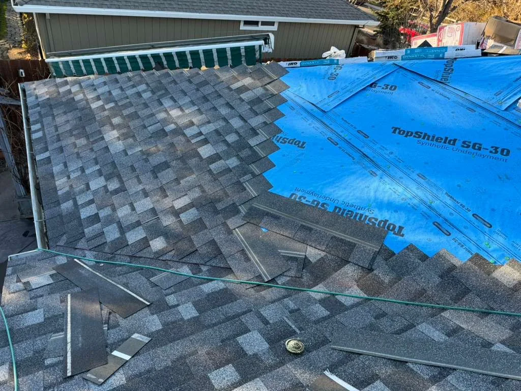 Partially completed roof with gray asphalt shingles installed on one section and blue synthetic underlayment on the other.