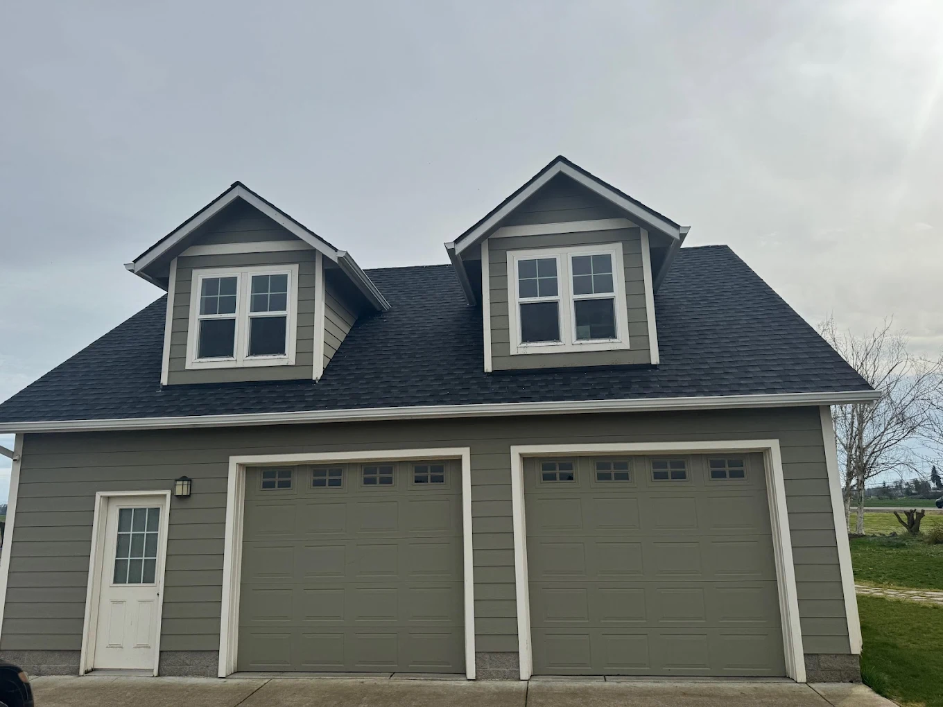 Two-car garage with olive-green doors, white trim, and two dormer windows above.