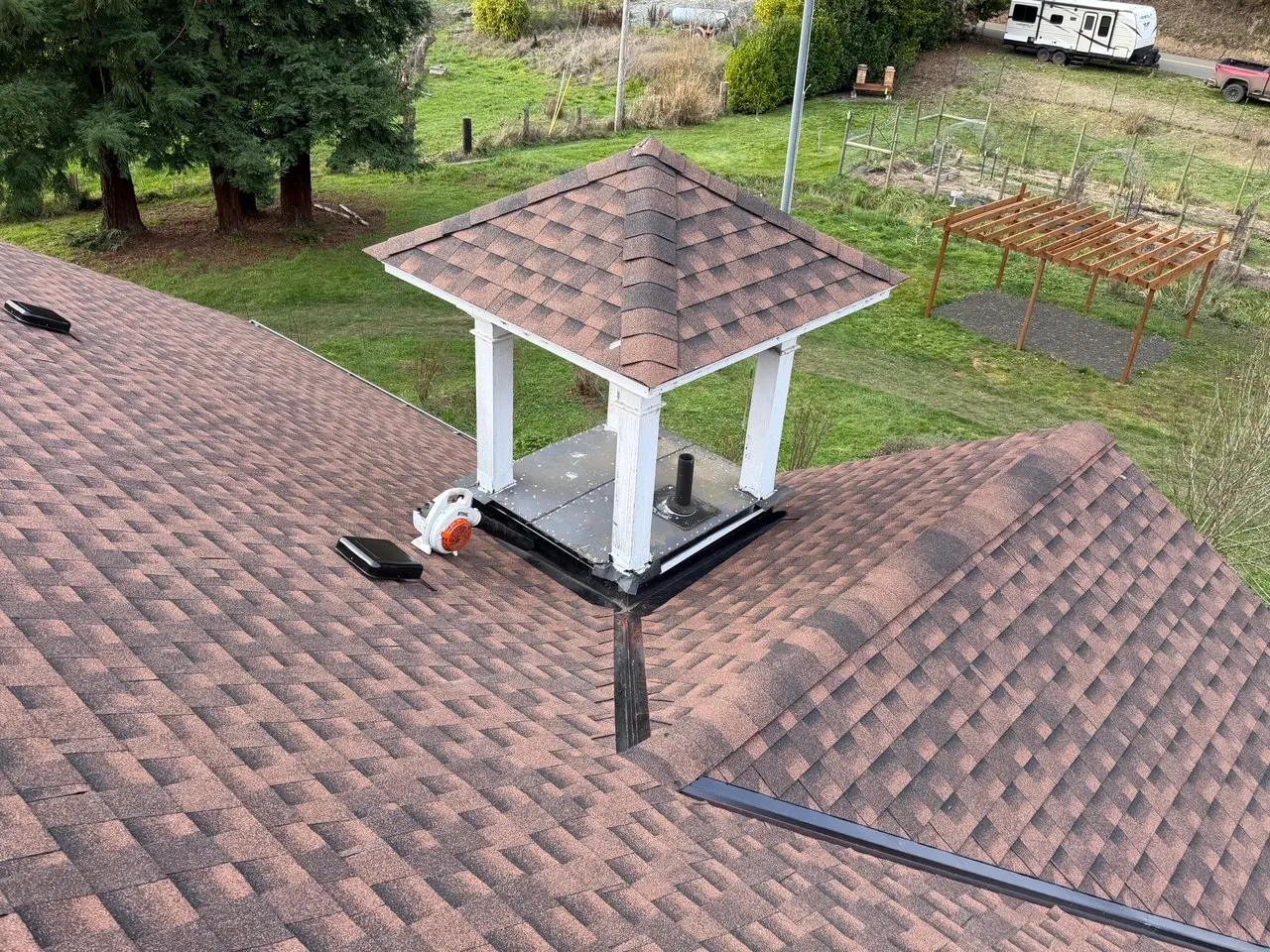 Brown shingled roof with a small white square cupola supported by four columns and a black vent pipe underneath.